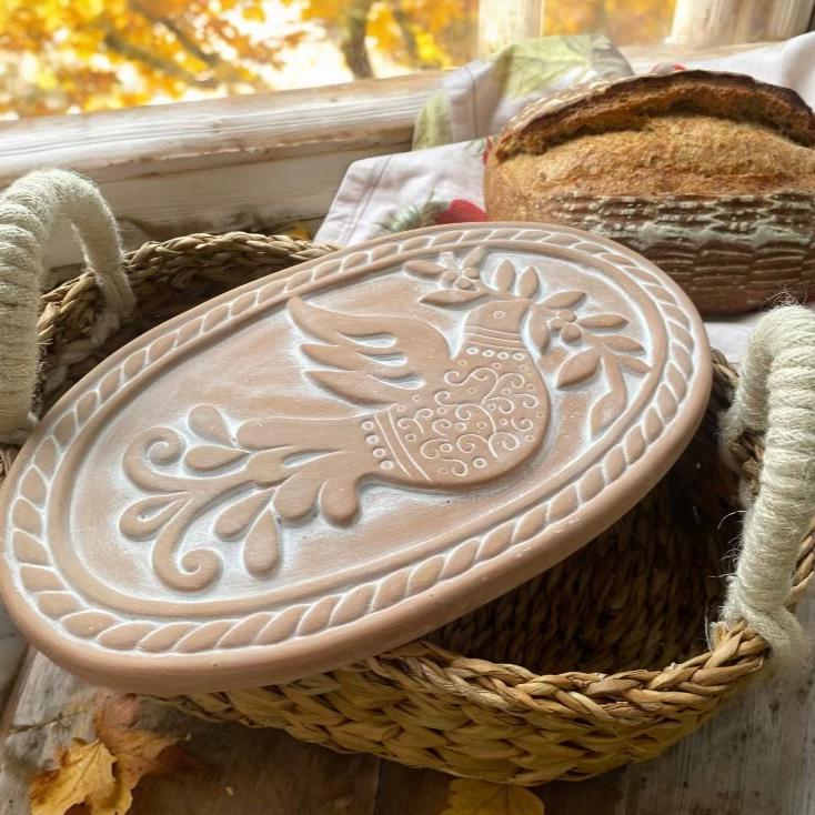 Handcrafted terracotta bread warmer in seagrass basket on rustic kitchen table with fall decor, perfect for keeping bread warm during autumn gatherings.